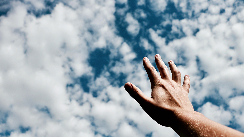 handing reaching toward blue sky with clouds