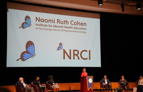 stage with large naomi ruth cohen logo displayed on screen behind them