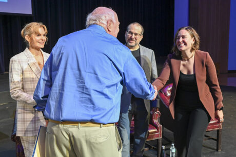older man in blue shirt shaking hands with people on stage