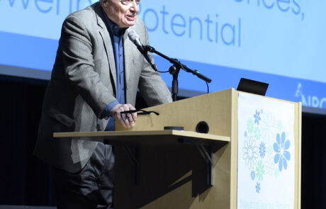 older man in sport coat speaking on stage behind a podium