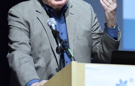older man in sport coat speaking on stage behind a podium