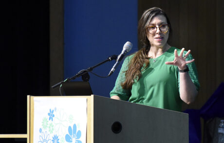 woman with glasses and green outfit speaking on stage behind a podium
