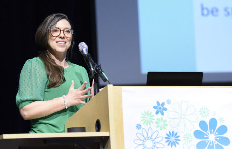 woman with glasses and green outfit speaking on stage behind a podium