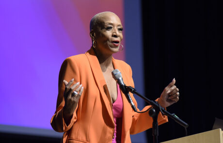 woman in orange business attire speaking on stage behind a podium