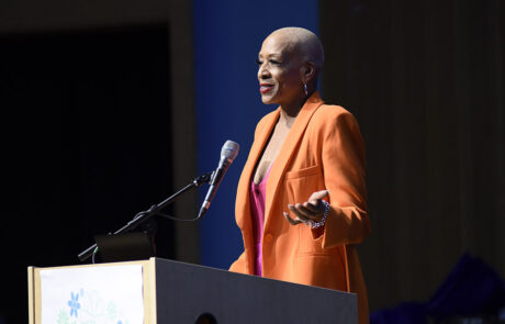 woman in orange business attire speaking on stage behind a podium