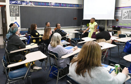 woman in lime green vertically striped dress speaking with people in classroom